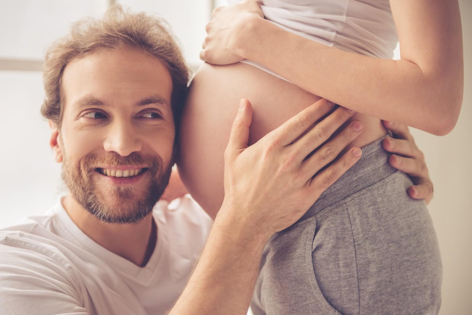 Ein Mann und werdender Vater hält sein Ohr an den Babybauch seiner Partnerin © Shutterstock