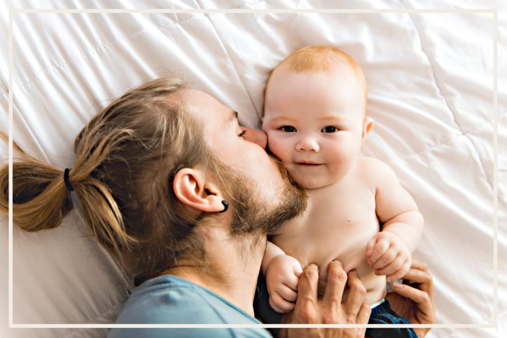 Ein Mann und junger Vater liegt auf dem Bett und küsst sein Baby © Shutterstock